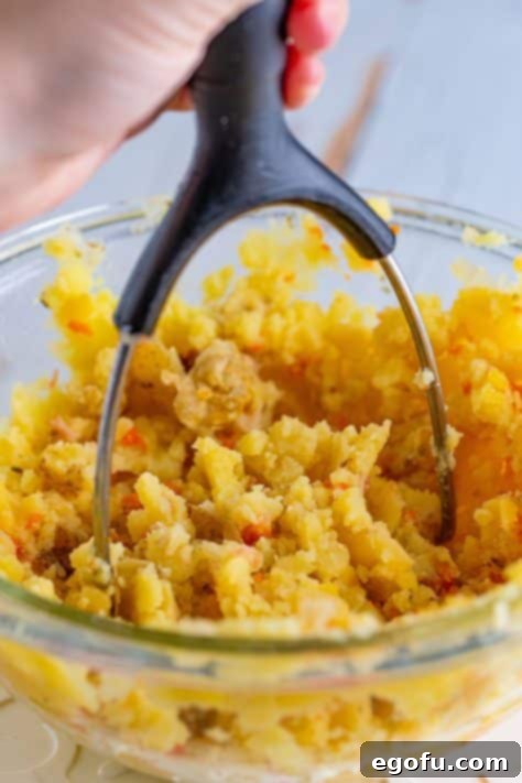 Cooked potatoes being mashed by a potato masher.