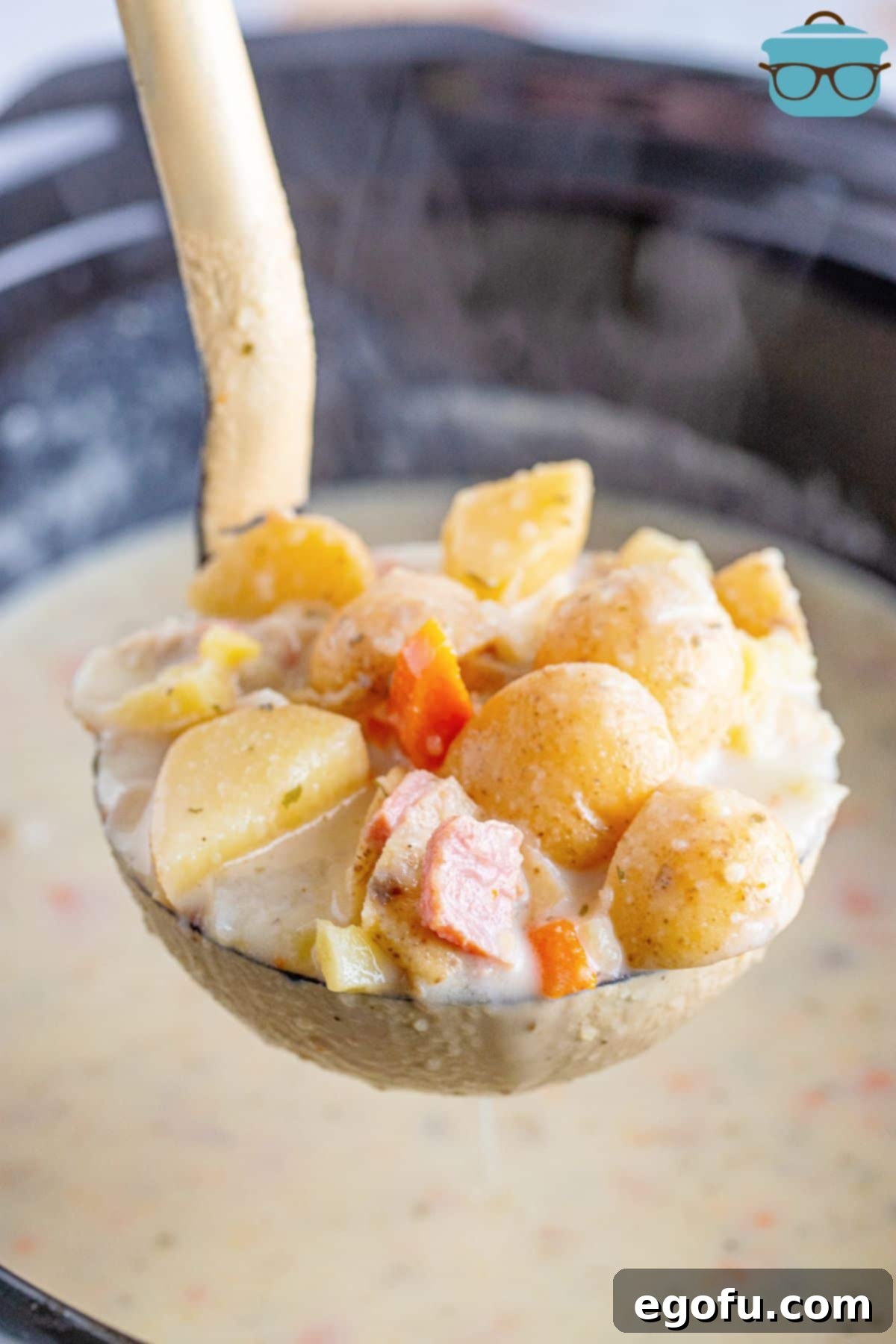 A ladle of Crock Pot Potato and Ham Soup held above the rest of the batch.