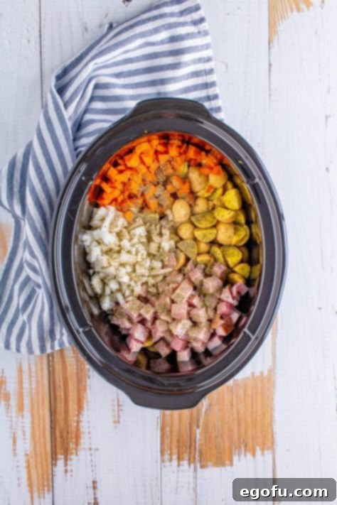 A crock pot with thyme, parsley, pepper, onion, carrots, ham, and potatoes.