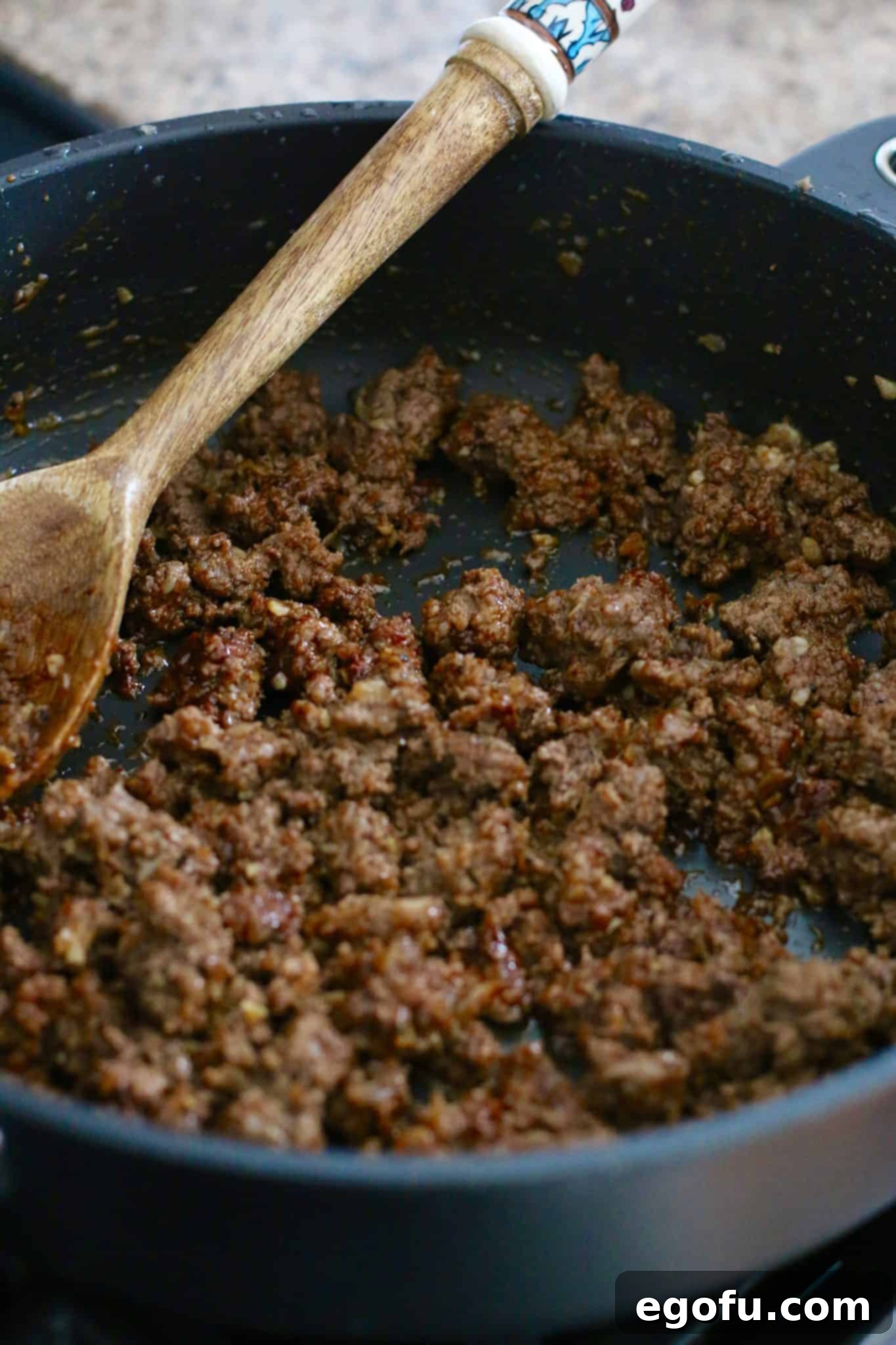 Fully cooked taco ground beef with a wooden spoon in a black skillet, perfectly seasoned and ready for the next step.