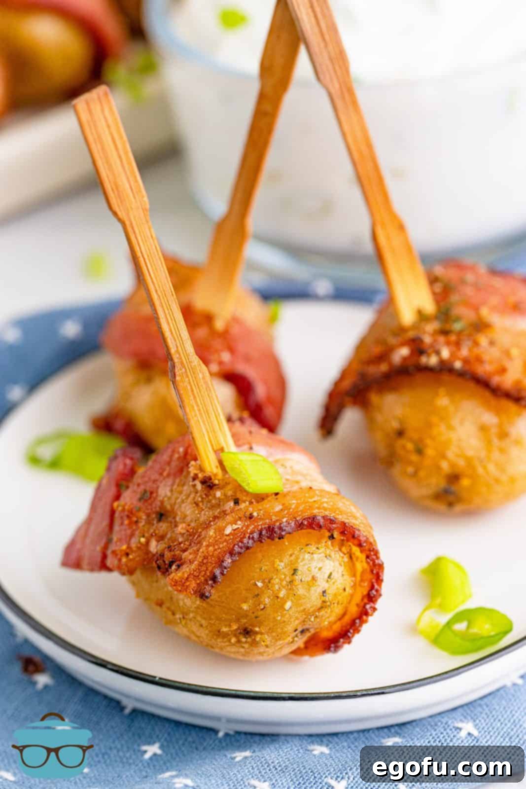 Three bacon wrapped potatoes on a small white appetizer plate, garnished with fresh herbs.