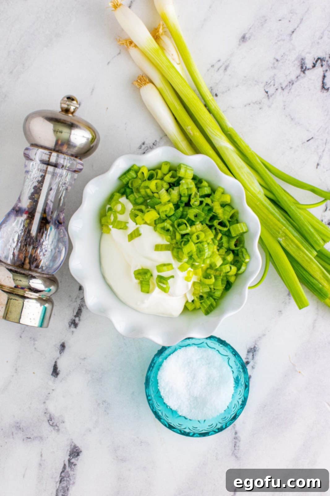 A bowl of sour cream mixed with sliced green onions, with salt and pepper shakers in the background.