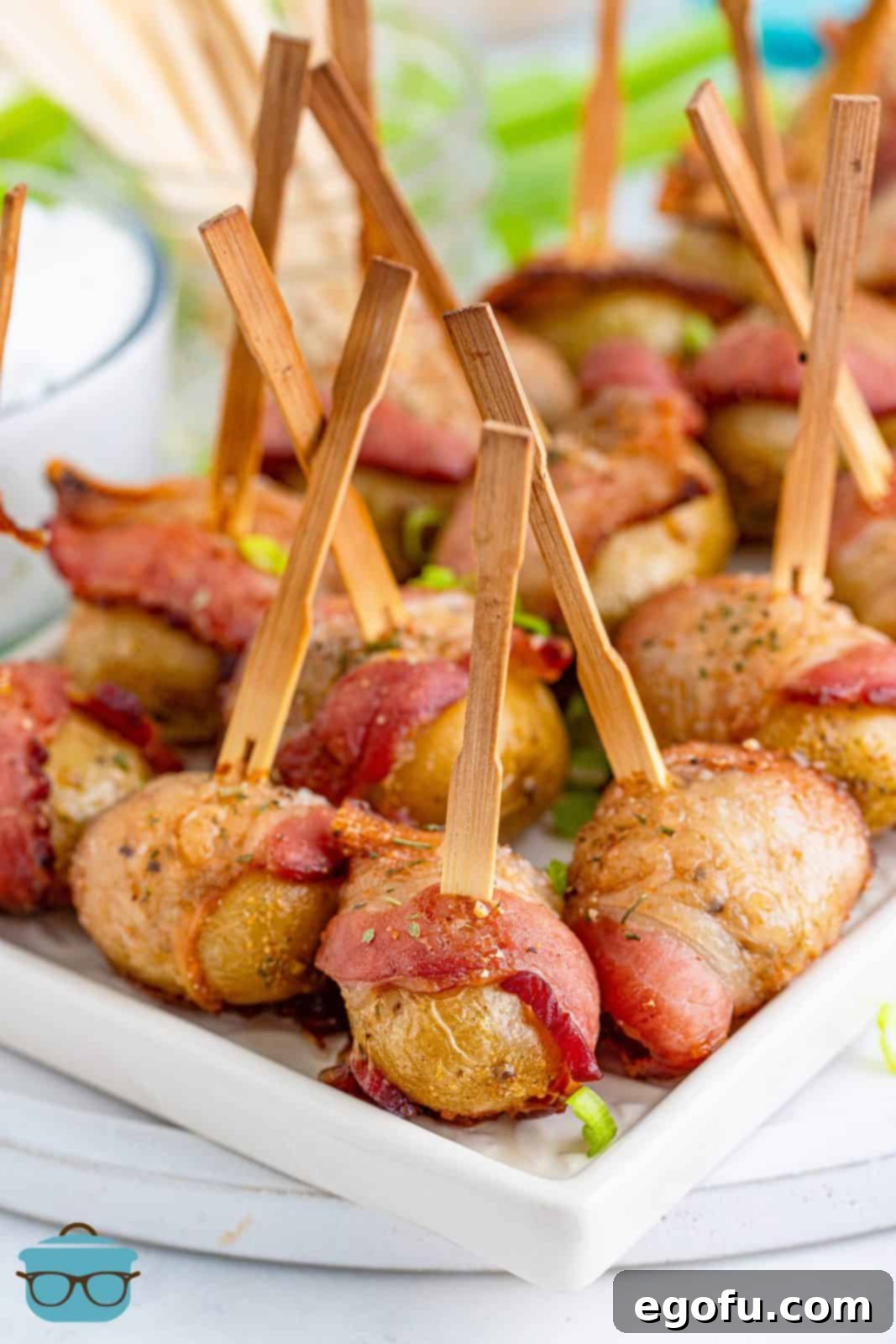 A white serving tray holding several bacon-wrapped potatoes with toothpicks, ready to be served.