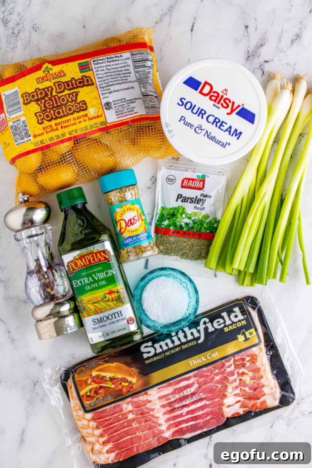 A selection of ingredients laid out: baby potatoes, thick-cut bacon, olive oil, garlic and herb seasoning, kosher salt, fresh black pepper, sour cream, and green onions.