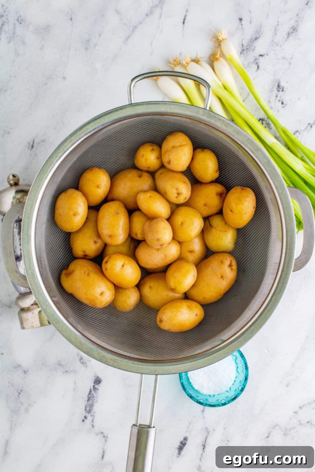 Baby potatoes being drained in a colander after parboiling, steam gently rising.