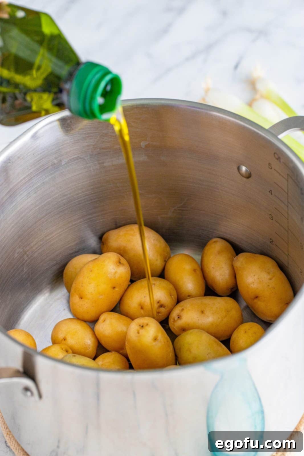 Olive oil being poured over warm, parboiled baby potatoes in a pot, ready for seasoning.