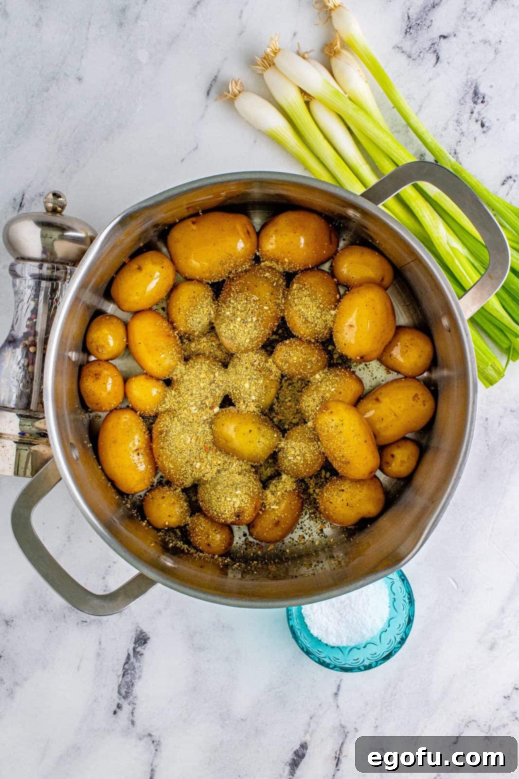 Garlic and herb seasoning sprinkled over olive oil-coated baby potatoes in a pot.