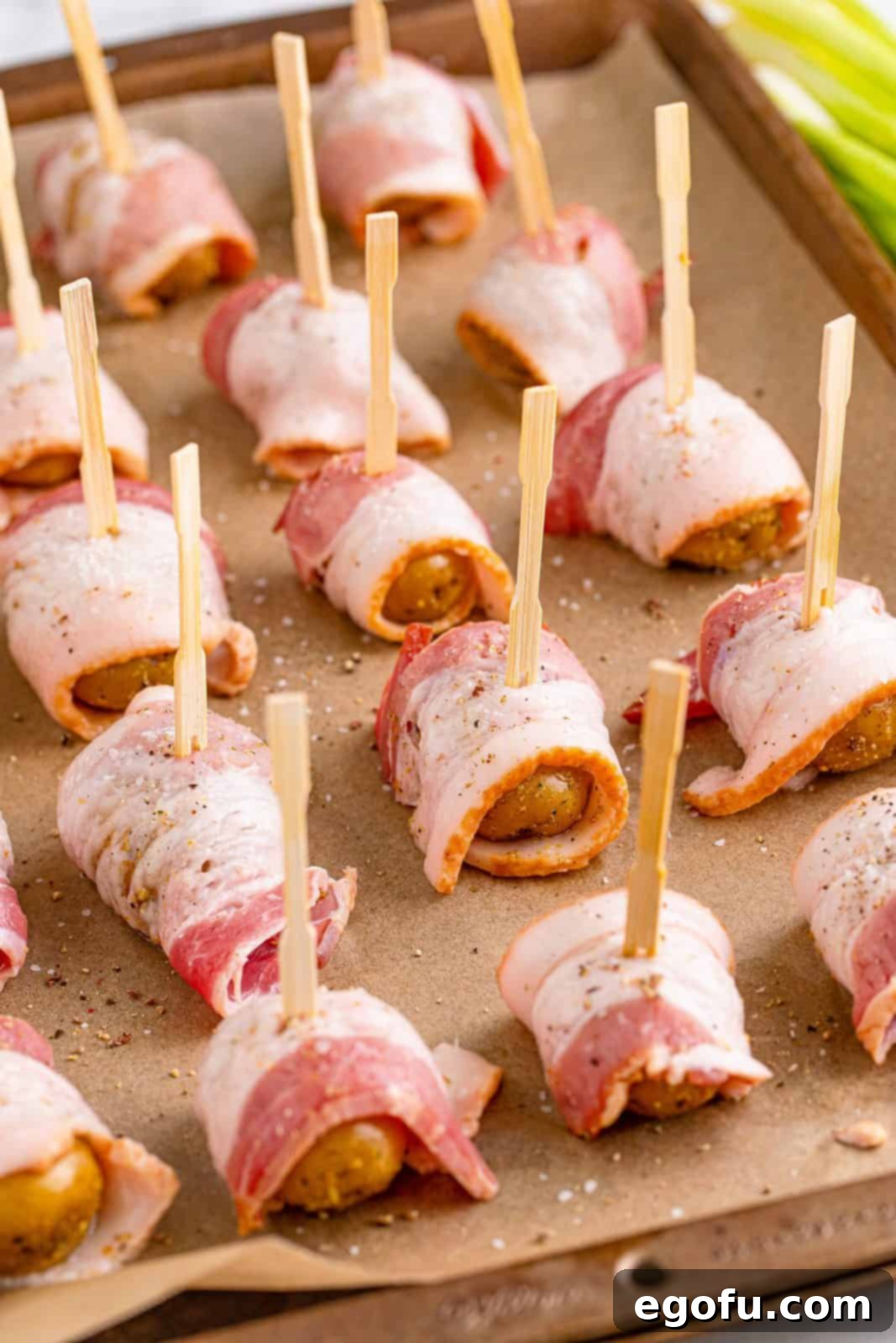Bacon-wrapped baby potatoes, secured with toothpicks, neatly arranged on a parchment-lined baking sheet.