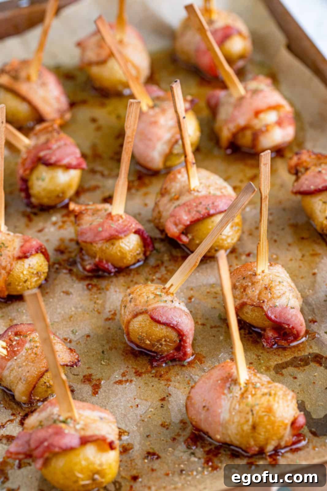 Fully cooked and crispy bacon-wrapped potatoes fresh out of the oven, on a baking sheet.