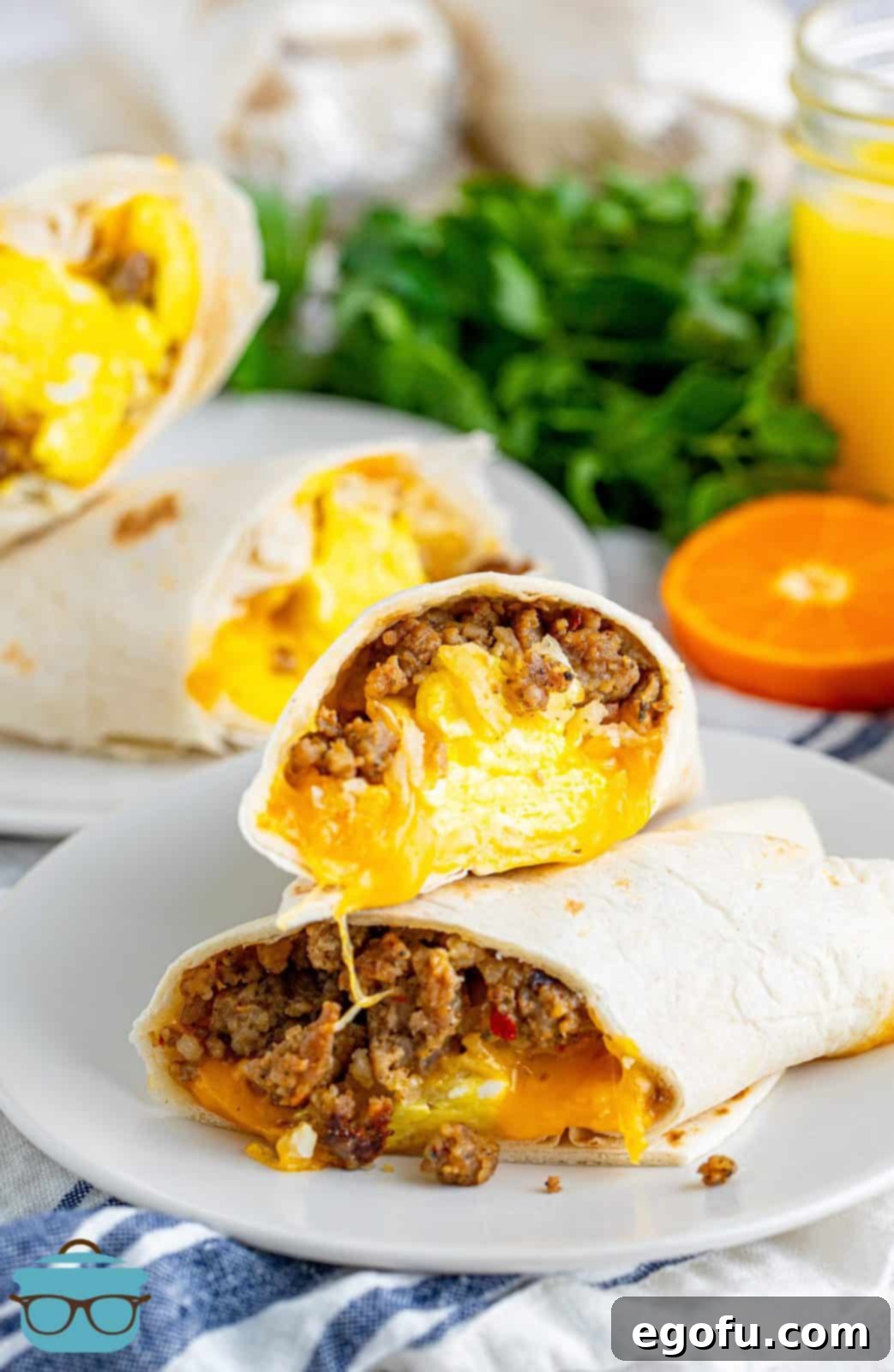 Two halves of a breakfast burrito, stacked, showcasing the layers of sausage, egg, cheese, and hash browns, served on a white plate.