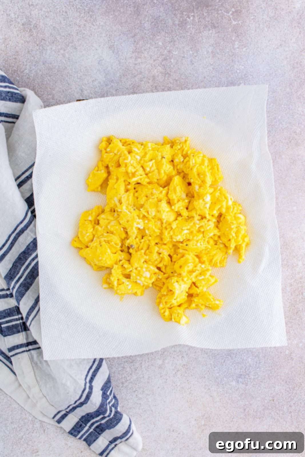 Scrambled eggs, light and fluffy, placed on a paper towel to cool slightly before being added to the burritos.