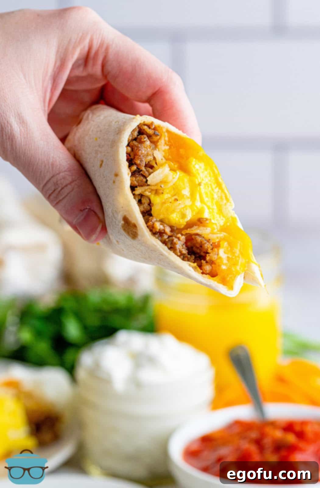A hand holding up one half of a freshly reheated breakfast burrito, showcasing its delicious layers, ready to be enjoyed.