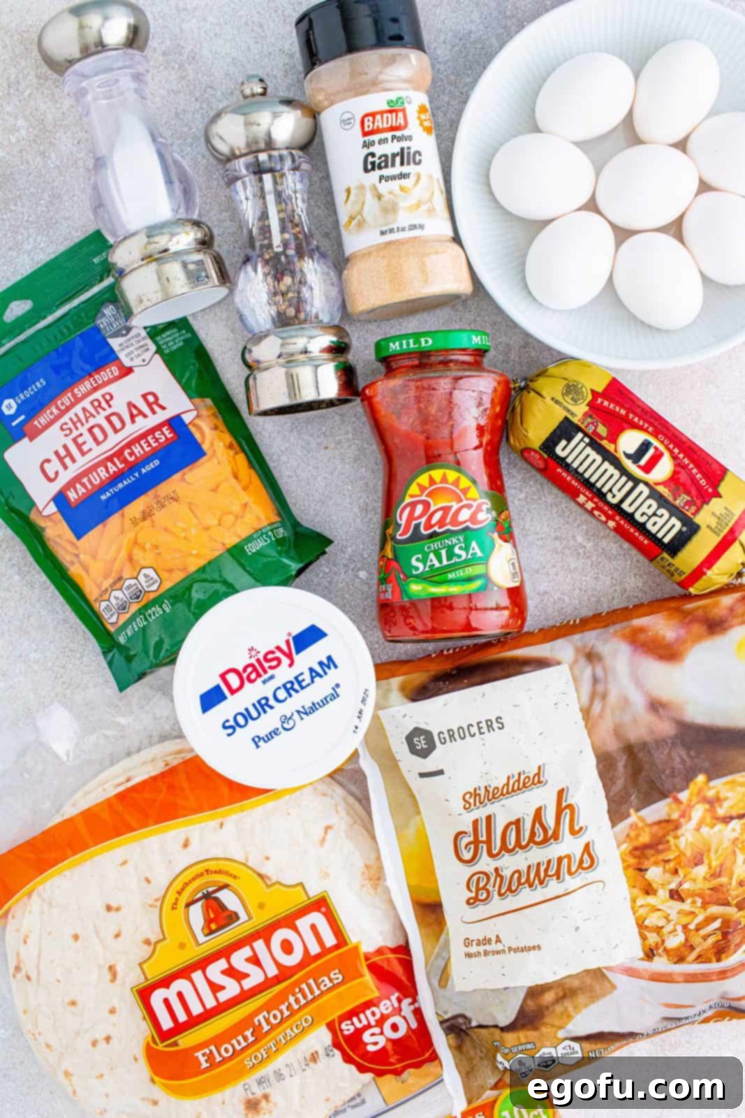 A flat lay of all the fresh ingredients: flour tortillas, eggs, cheese, ground sausage, and shredded hash browns, ready for cooking.