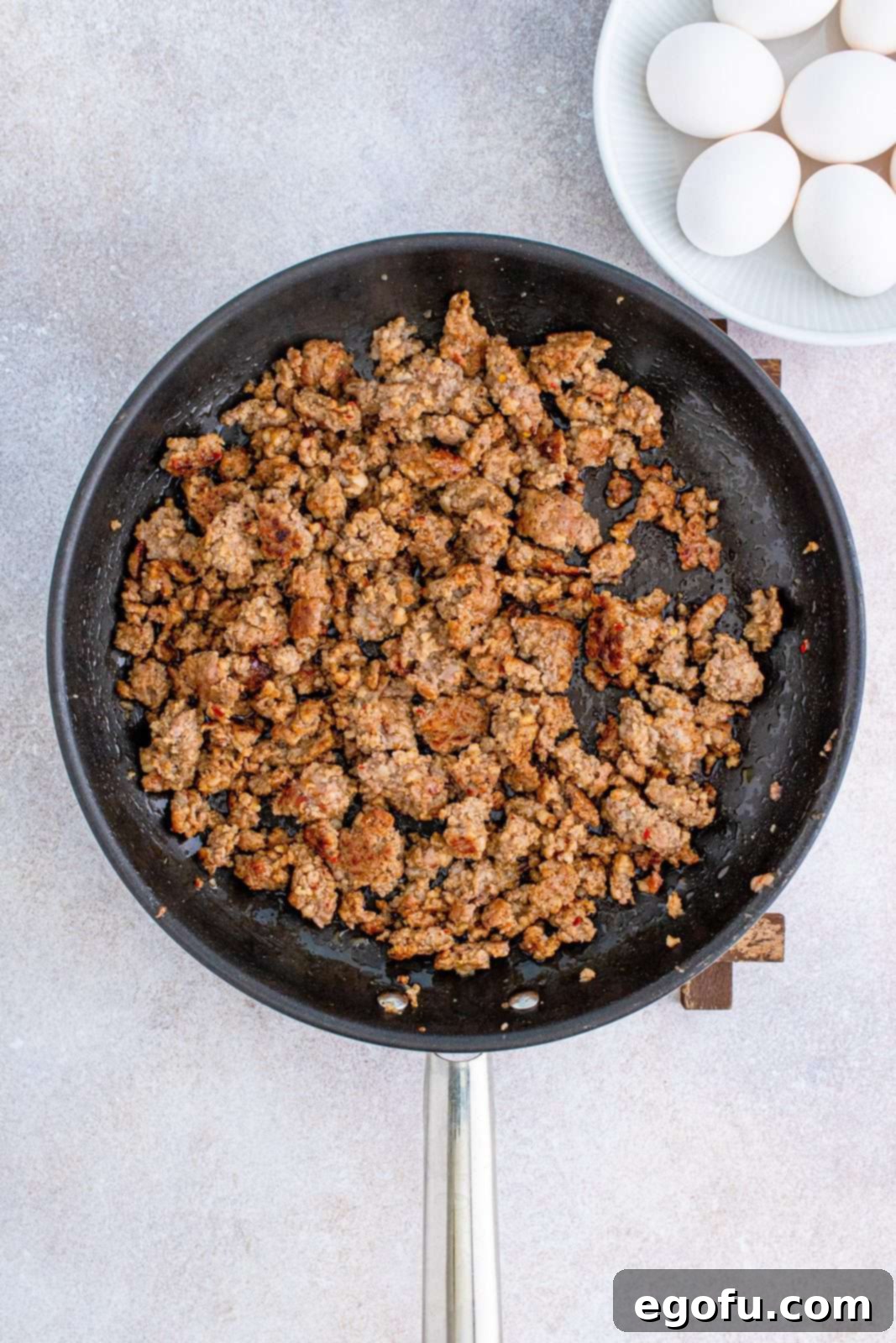 Close-up of cooked and crumbled ground sausage sizzling in a large skillet, golden brown and ready to be drained.