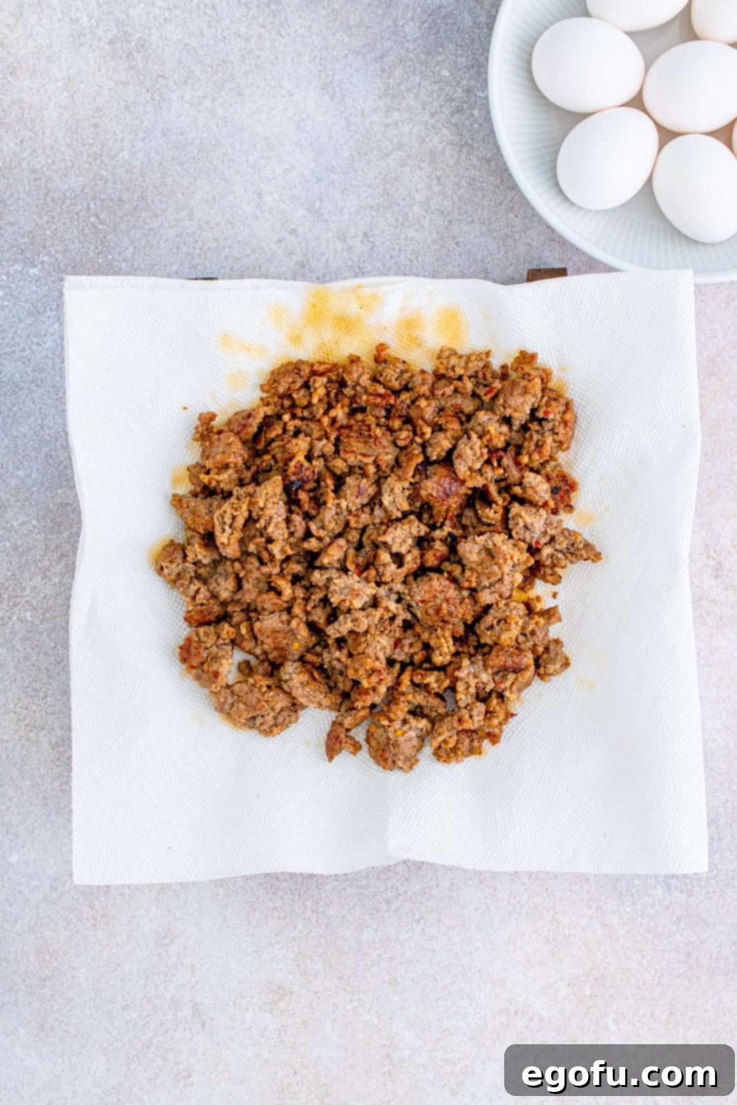 A spatula pressing cooked ground sausage onto a paper towel-lined plate to drain excess grease after browning.