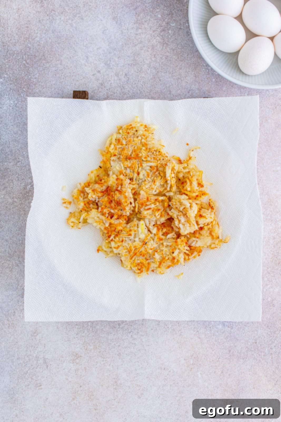 Crispy, golden-brown shredded hash browns resting on a paper towel-lined plate after being cooked, ready for assembly.