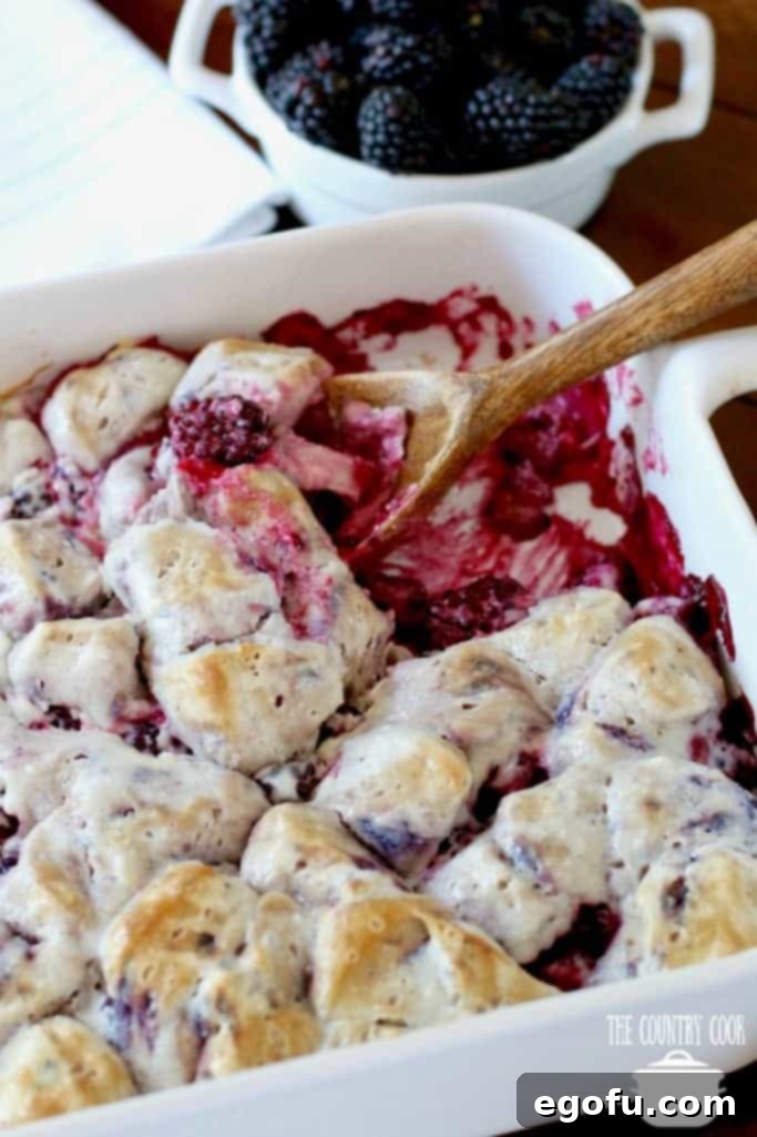 Blackberry Burst Bake 13 Blackberry Bubble Up baked in a casserole dish with a wooden spoon scooping out a serving.