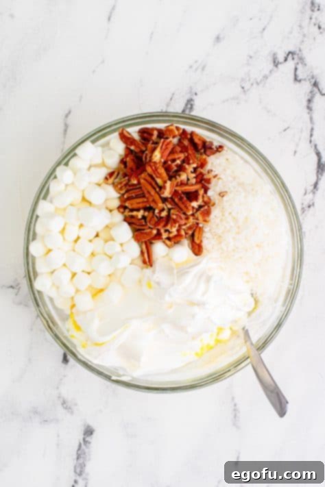 Tropical Cloud Delight 11 Mini marshmallows, chopped pecans, and Cool Whip added to pineapple in a clear bowl for gentle mixing.