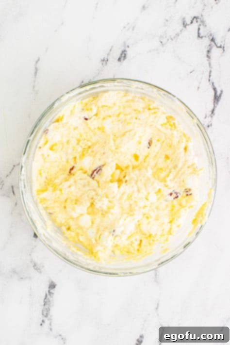 Tropical Cloud Delight 12 Fully combined pineapple fluff in a clear bowl on a marble surface, ready for chilling.