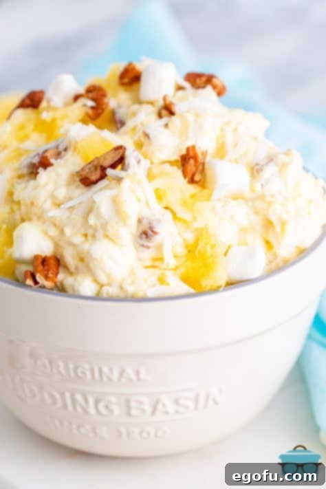 Tropical Cloud Delight 13 Pineapple fluff, topped with chopped pecans in a white serving bowl on a white wood surface, ready to be served.