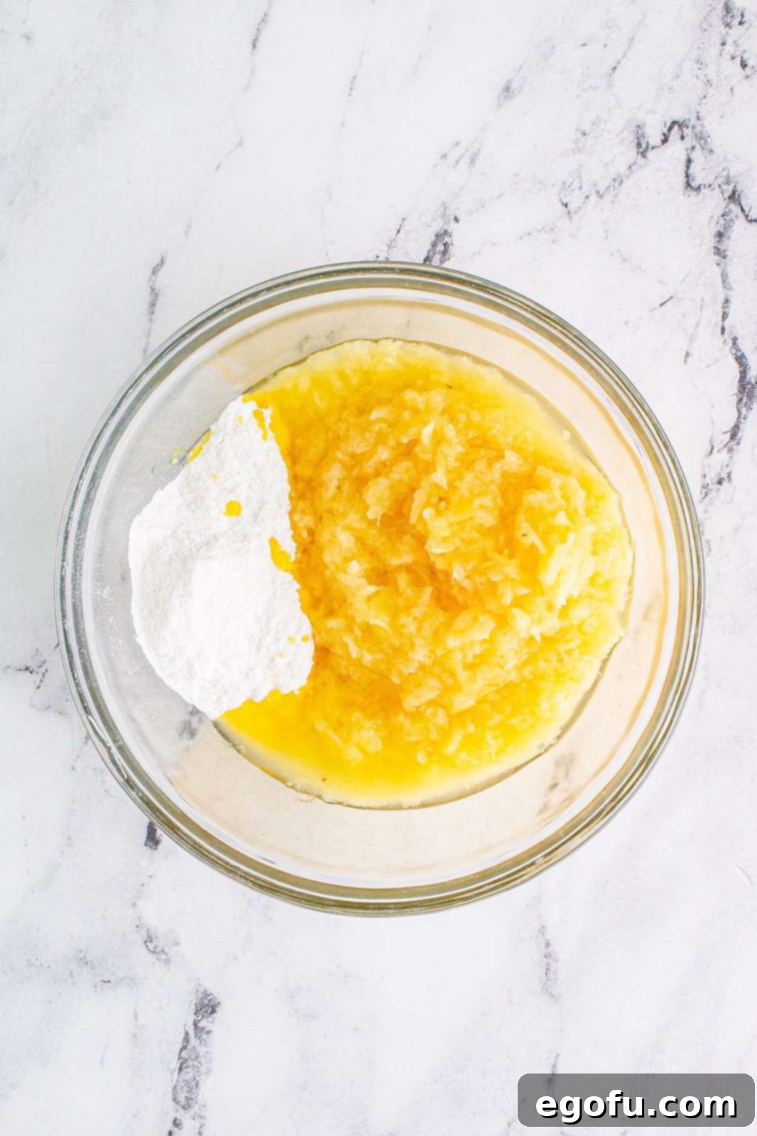 Tropical Cloud Delight 5 Instant vanilla pudding mix and a can of crushed pineapple being stirred together in a clear mixing bowl, showing the initial stage of combining the ingredients.