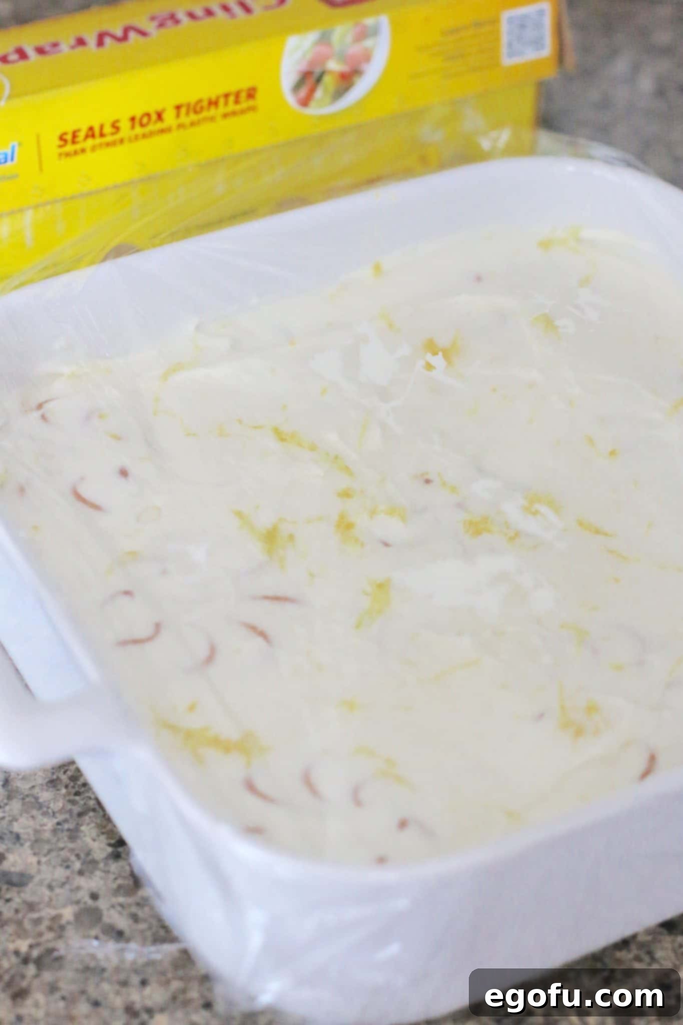 Zesty Lemon No-Bake Delight 11 covering lemon icebox cake with Saran plastic wrap.