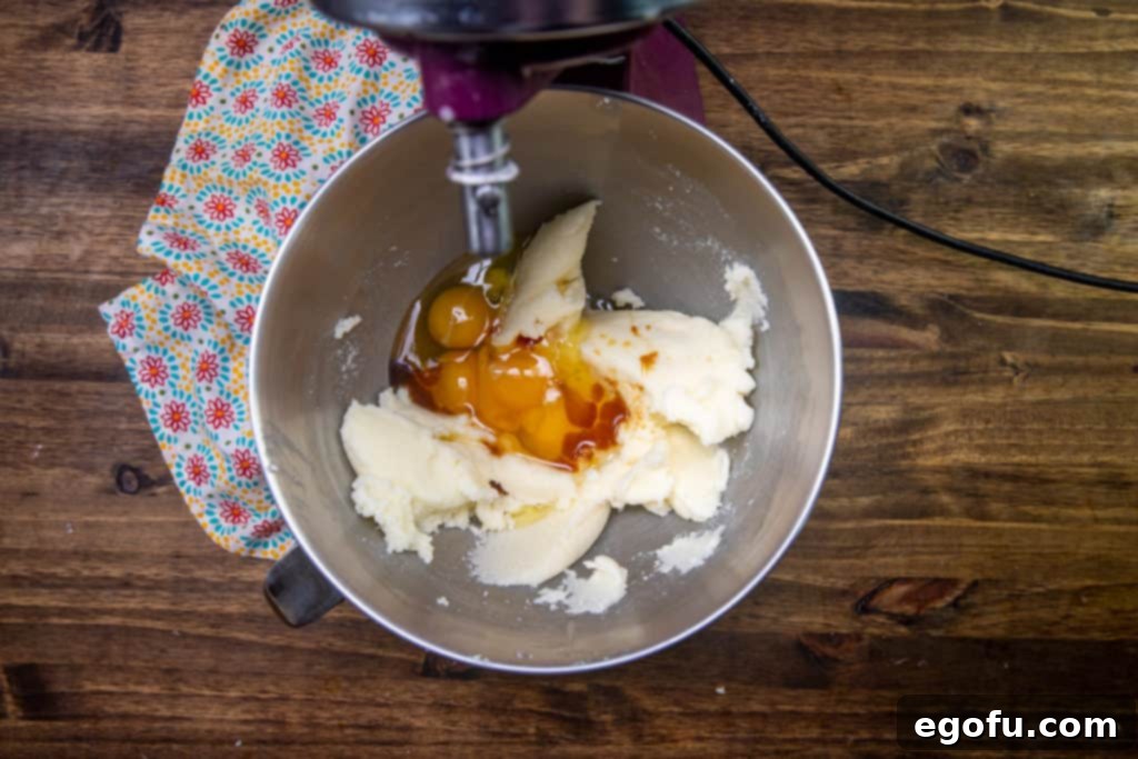 Velvet Peach Cream Bars 6 The mixing bowl now contains eggs and vanilla extract added to the creamed butter and sugar mixture, being beaten to ensure full integration and a smooth consistency.