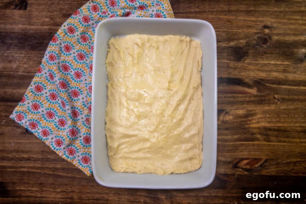 Velvet Peach Cream Bars 8 A smooth and even layer of cake batter is spread across the bottom of a rectangular baking pan, forming the crucial base for the layered Peaches and Cream Bars.