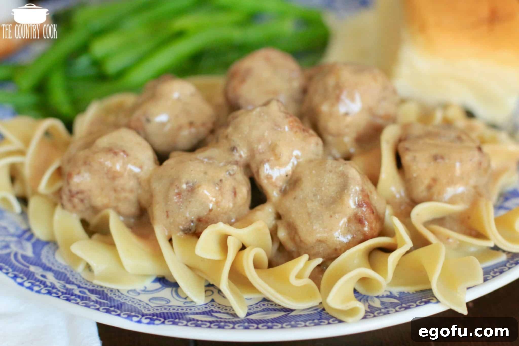 Slow Cooker Swedish Meatballs and Gravy served over egg noodles with a side of green beans and a dinner roll, ready to eat.
