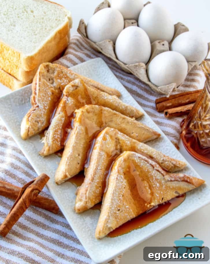 Pillowy French Toast Perfection 11 5 triangle slices of fluffy French toast lined up on a white tray with eggs in the background, ready to be served.