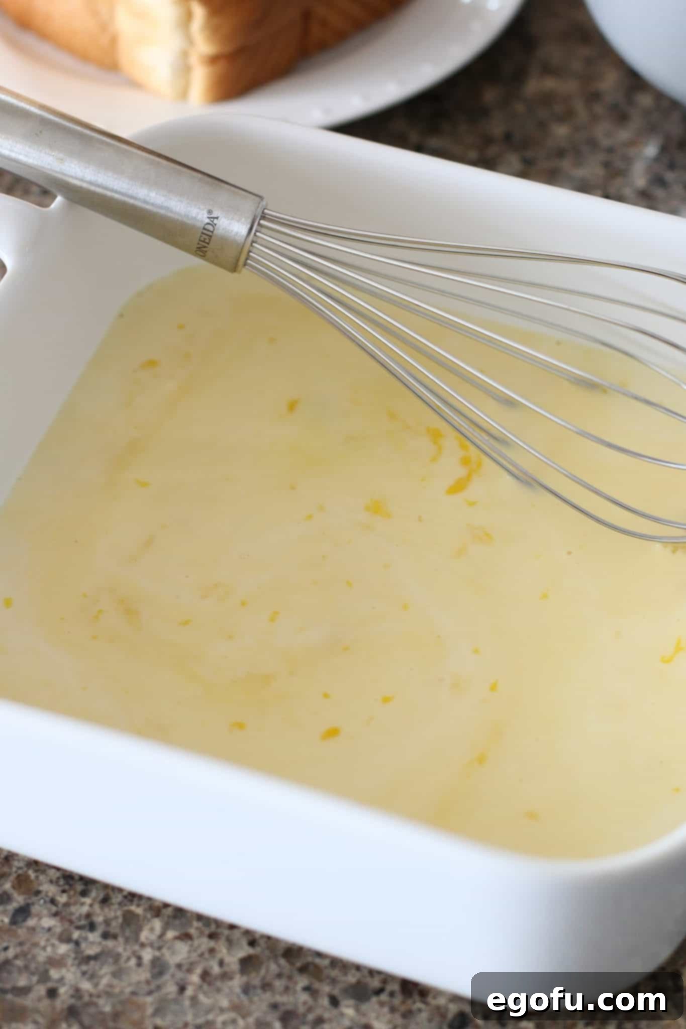 Pillowy French Toast Perfection 6 whisking eggs, milk, and vanilla extract until combined in a white square baking dish.