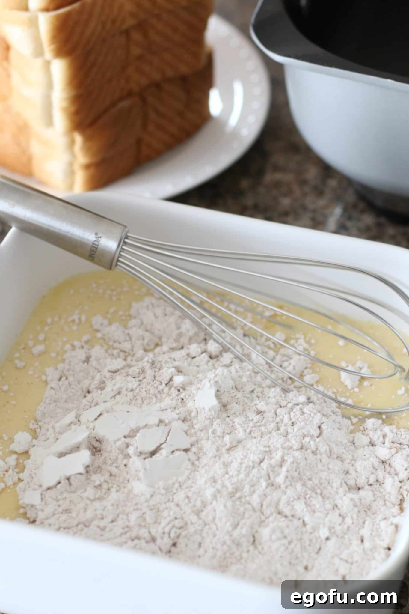 Pillowy French Toast Perfection 7 whisking flour and eggs together to form the pancake-like batter in a white square dish.