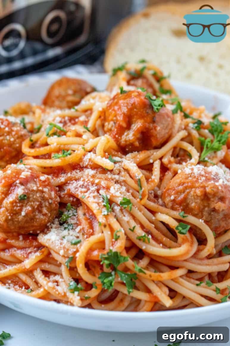 Effortless Slow Cooker Spaghetti and Meatballs 2 Close-up of perfectly cooked Crock Pot Spaghetti and Meatballs in a white bowl, ready to be served, with warm slices of bread in the background.