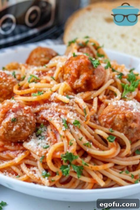 Effortless Slow Cooker Spaghetti and Meatballs 21 close up of Spaghetti and Meatballs in a white bowl with slices of bread in the background