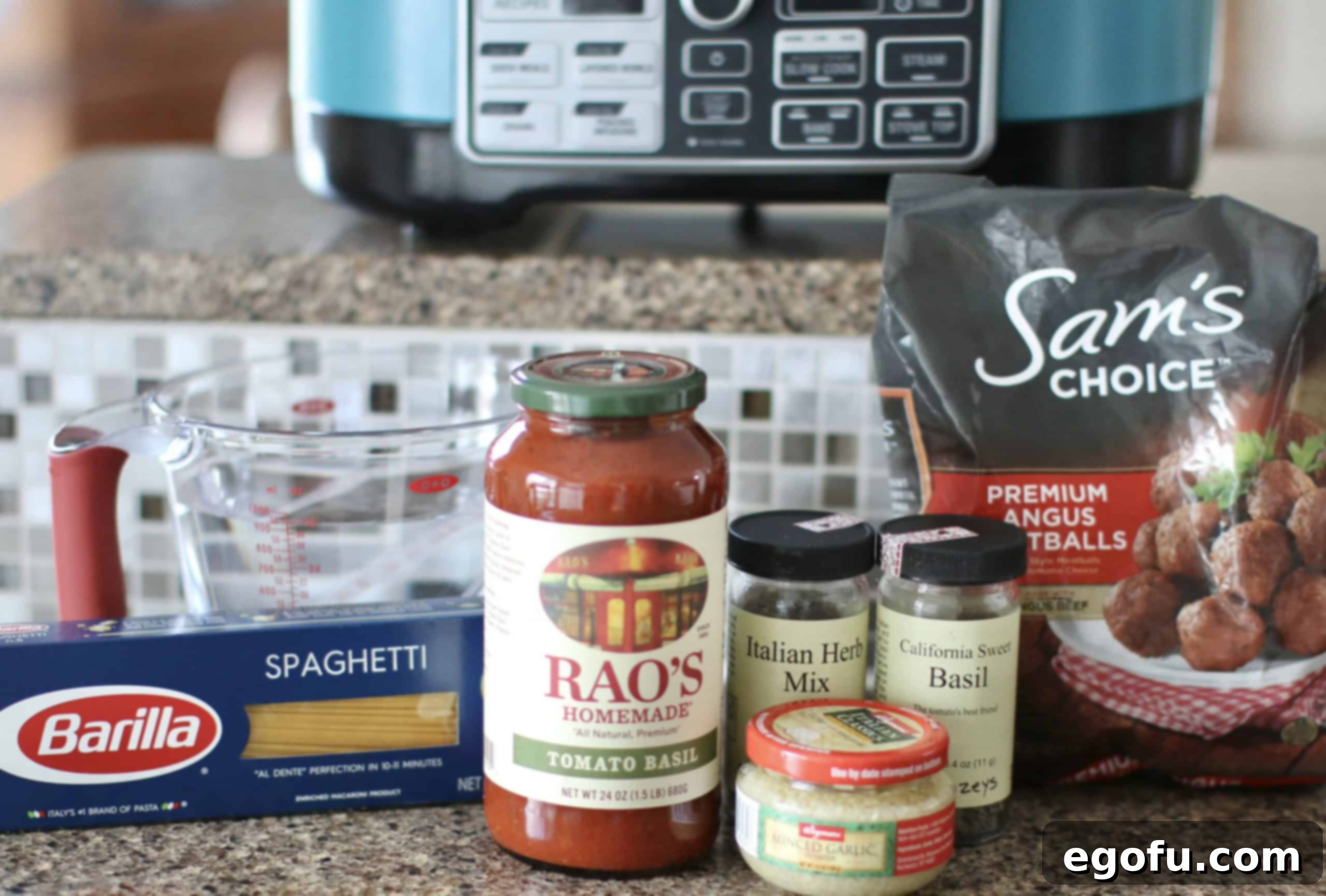 Effortless Slow Cooker Spaghetti and Meatballs 4 A flat lay photograph of all the ingredients needed for Crock Pot Spaghetti and Meatballs: spaghetti sauce, a bag of frozen meatballs, a glass of water, Italian seasoning, minced garlic, dried basil, uncooked spaghetti noodles, and a bottle of olive oil.