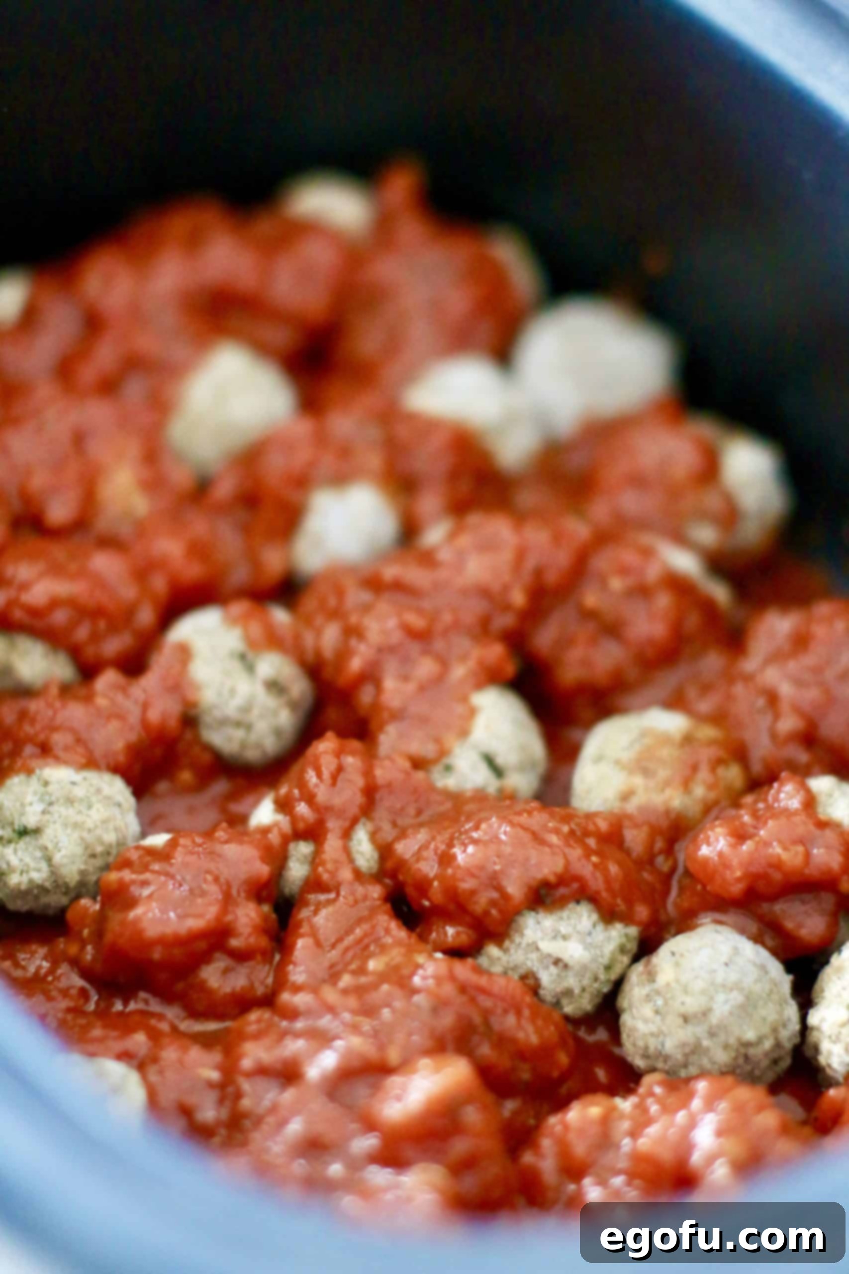 Effortless Slow Cooker Spaghetti and Meatballs 6 Spaghetti sauce being poured over frozen meatballs, creating a second layer of sauce in an oval slow cooker.