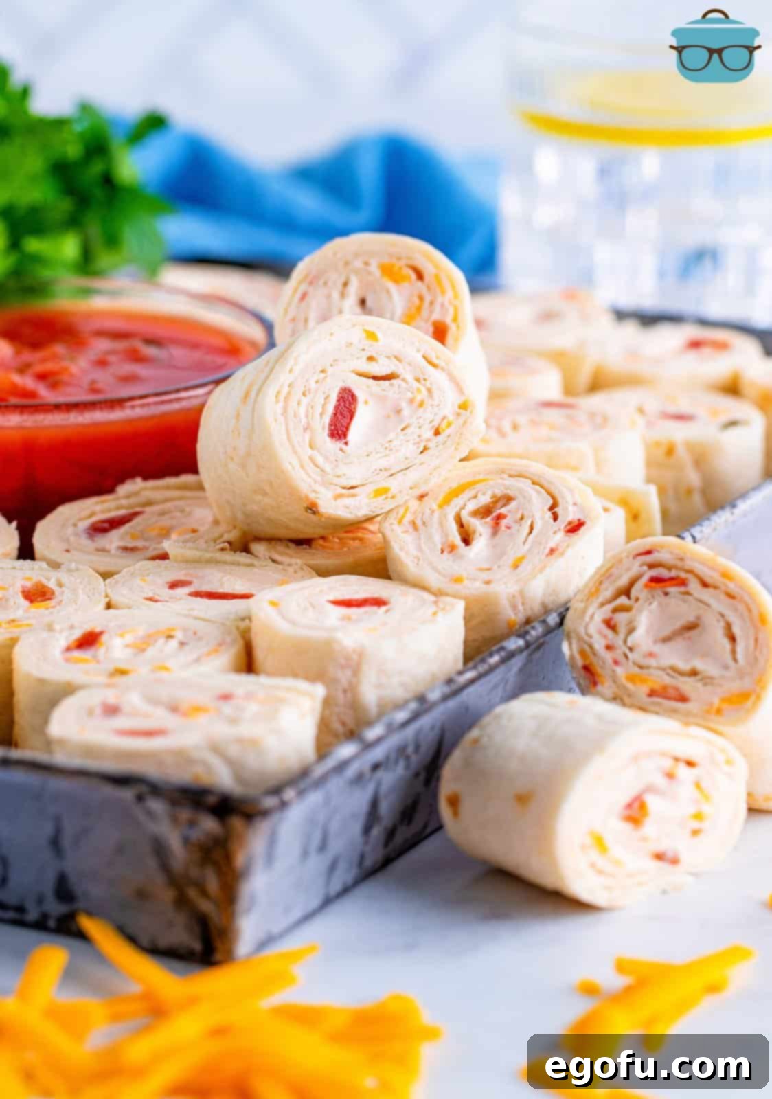 A selection of colorful Fiesta Pinwheels arranged on a metal serving tray, with a small bowl of red salsa positioned enticingly in the center, inviting guests to sample this festive appetizer.