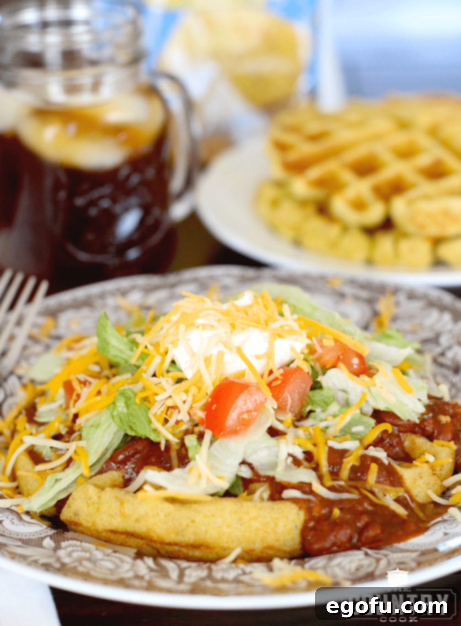 A beautifully presented Cornbread Waffles with Chili and Fixings on a stylish brown and white plate, with a fork neatly placed on the side, inviting you to dig in.