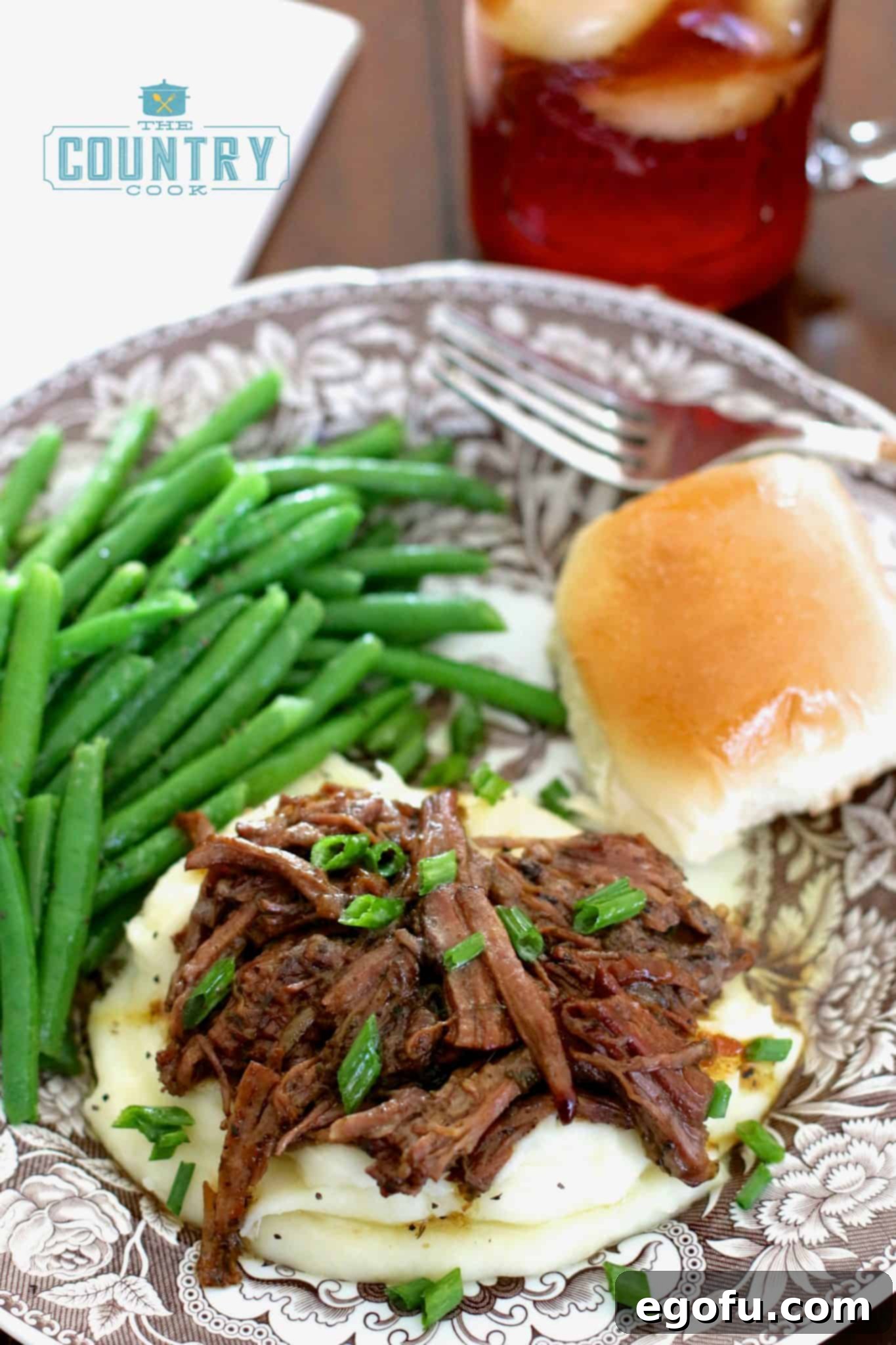 Mississippi pot roast shown plated onto some mashed potatoes with green beans and a roll.