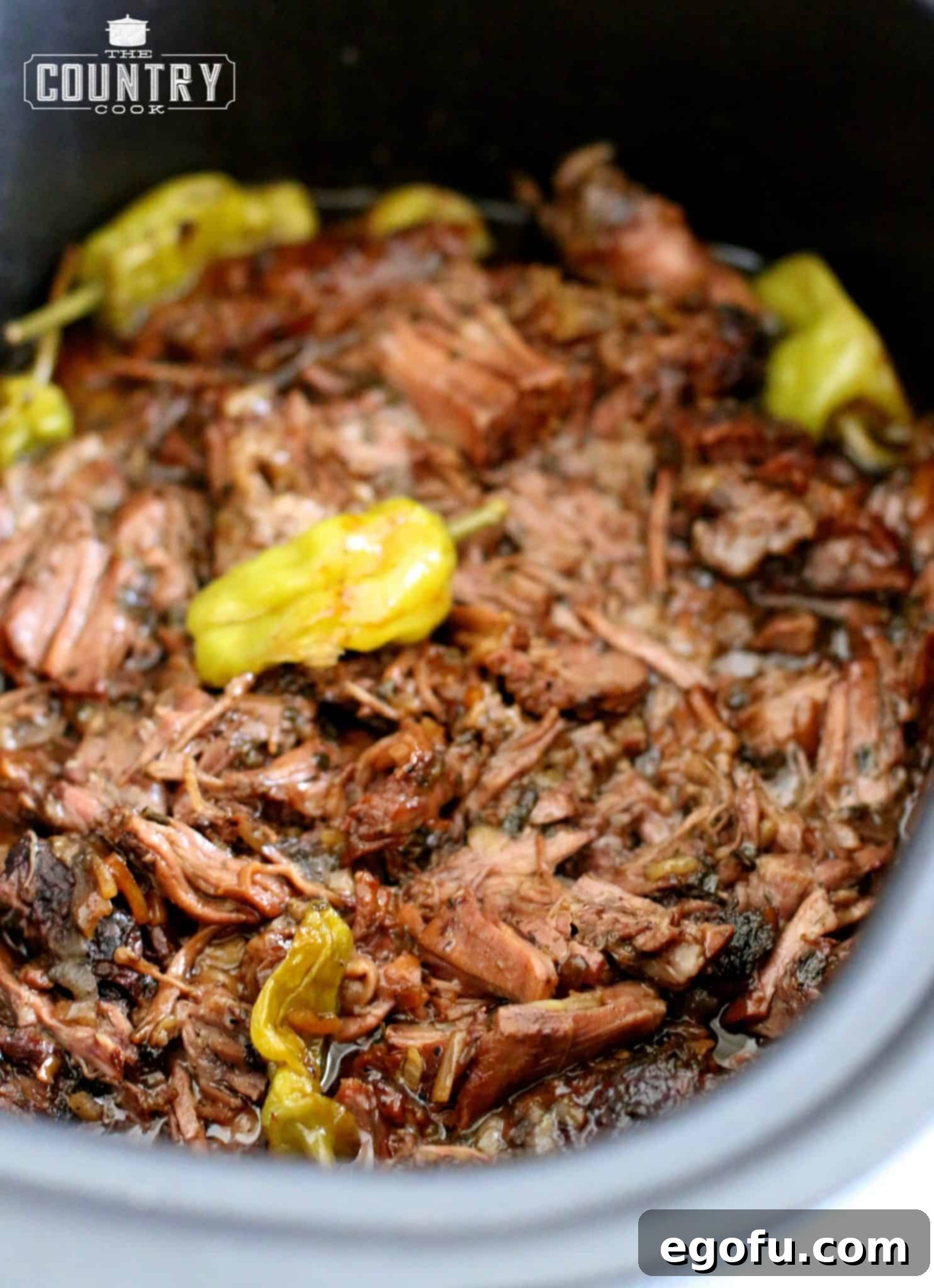 Fully cooked and shredded Mississippi pot roast in a slow cooker with peperoncini peppers on top.