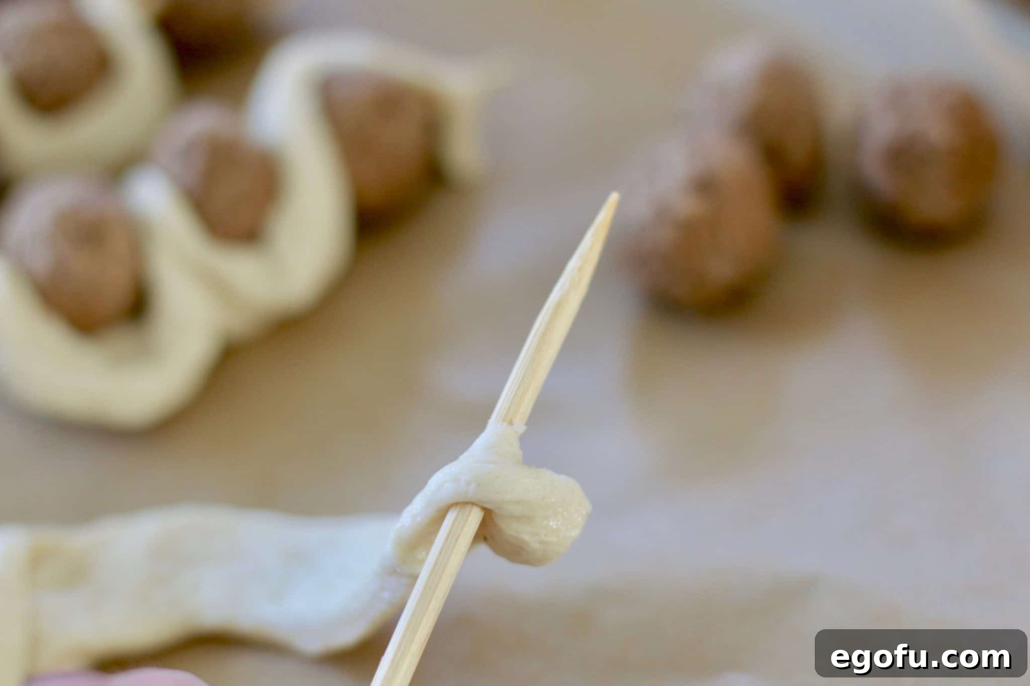 The initial step of threading breadstick dough and a single meatball onto a bamboo skewer.