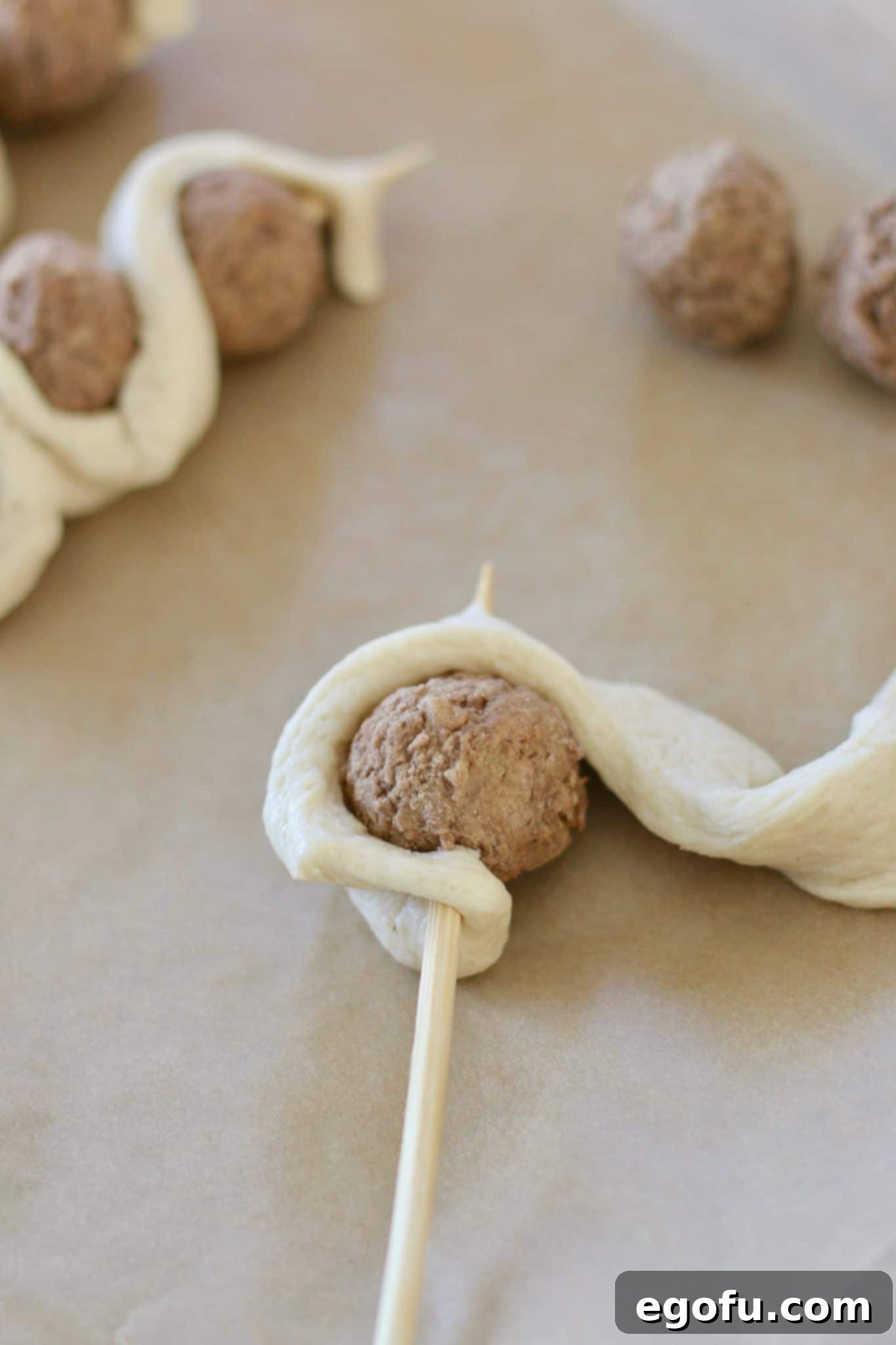 A bamboo skewer with three meatballs, each wrapped in breadstick dough, demonstrating the completed assembly before baking.