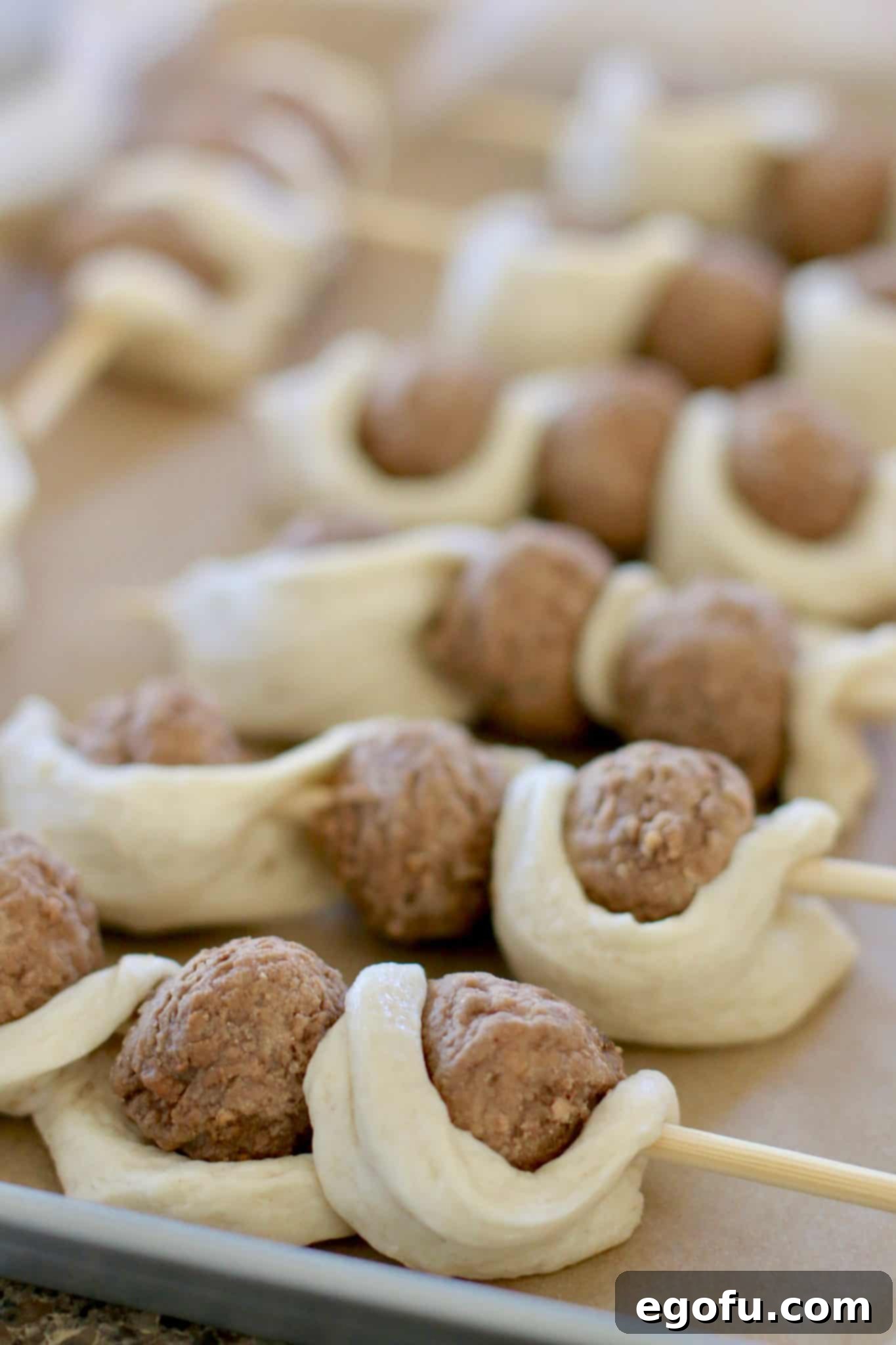 Multiple assembled meatball subs on sticks arranged neatly on a parchment-lined baking sheet, ready for the oven.