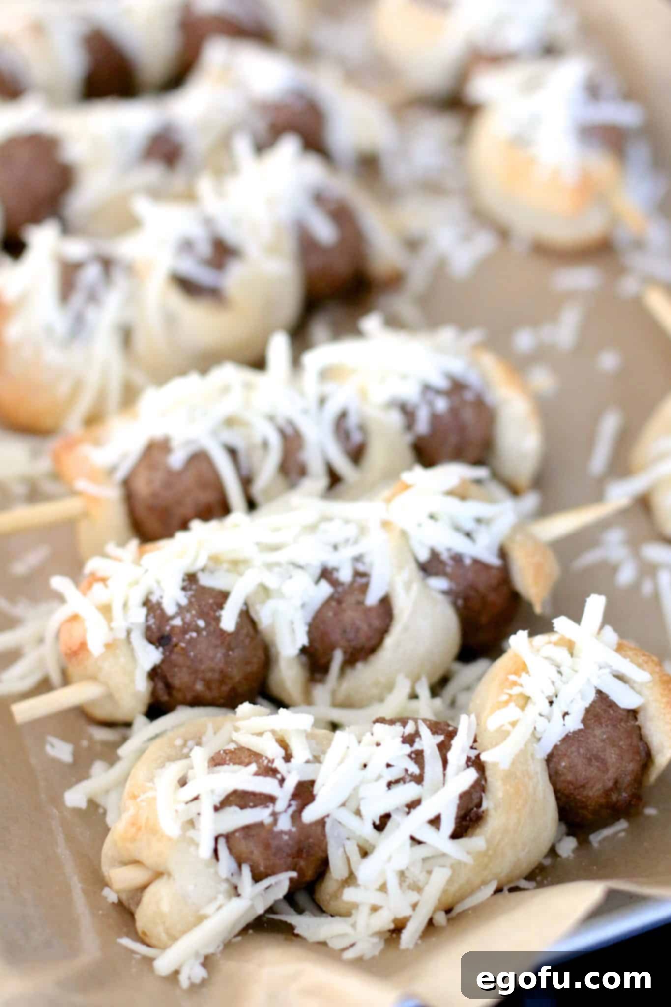 Sprinkling shredded mozzarella cheese and Italian seasoning over warm, baked meatball subs on sticks.