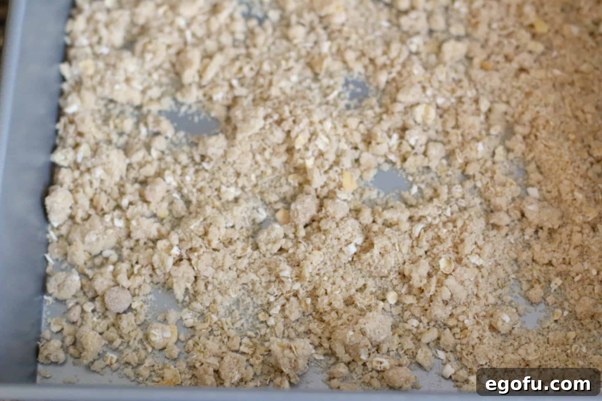 The crumb topping evenly spread on a small baking sheet, poised for its quick bake in the oven to achieve a golden, crunchy texture.