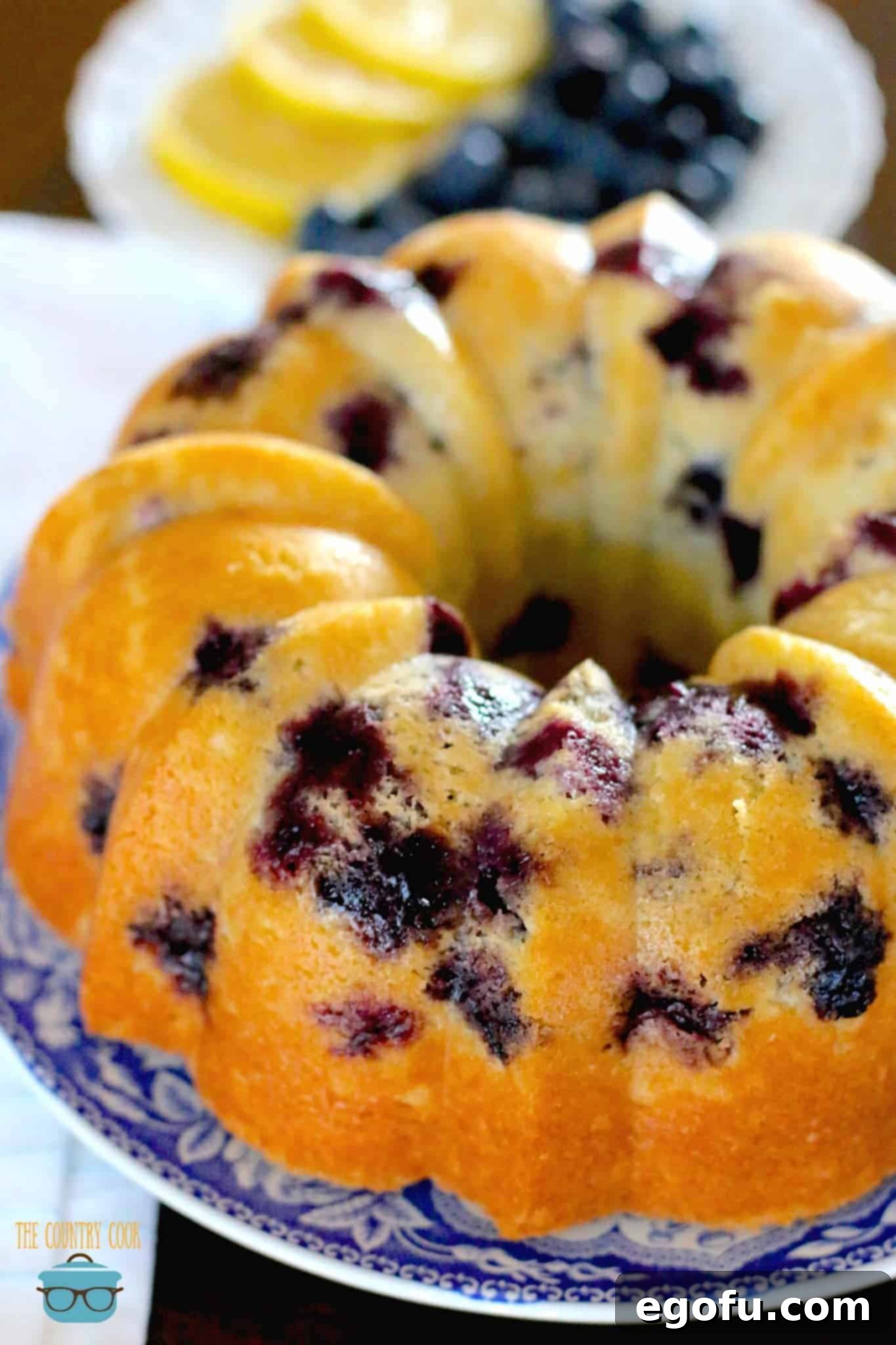 The fully baked Blueberry Muffin Bundt Cake, beautifully released from its pan, showcased on an elegant blue and white serving plate.