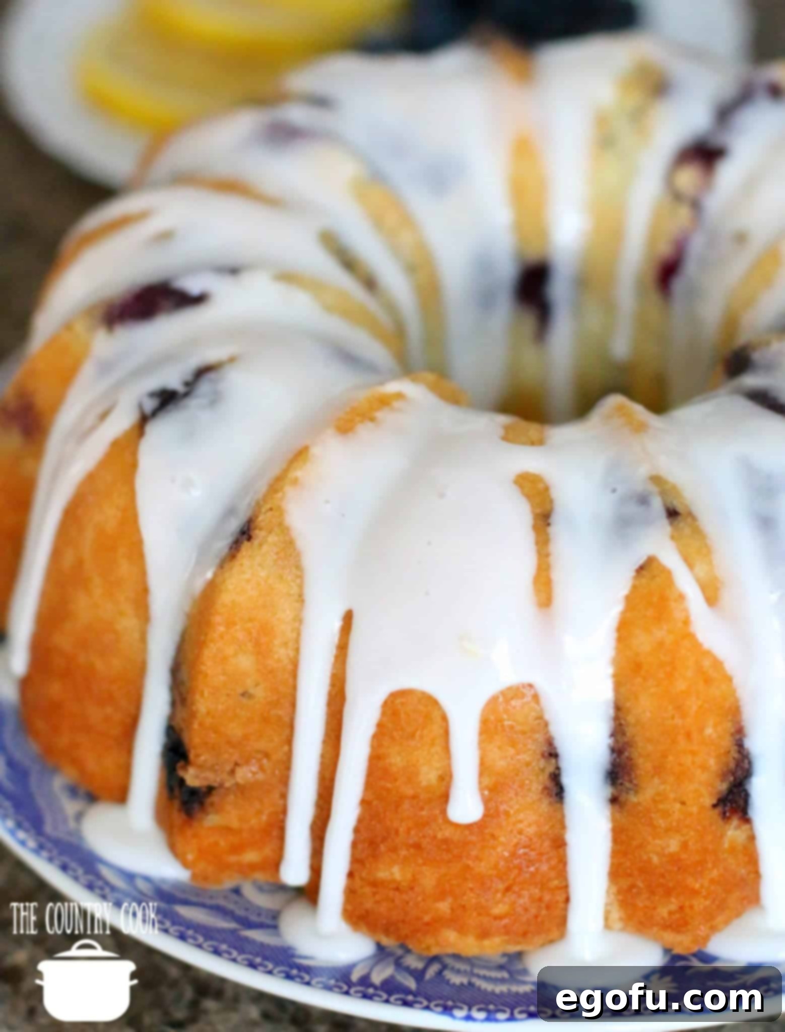 A stunning Fresh Blueberry Muffin Cake adorned with a generous drizzle of glistening lemon icing, enhancing its visual appeal and fresh flavor.