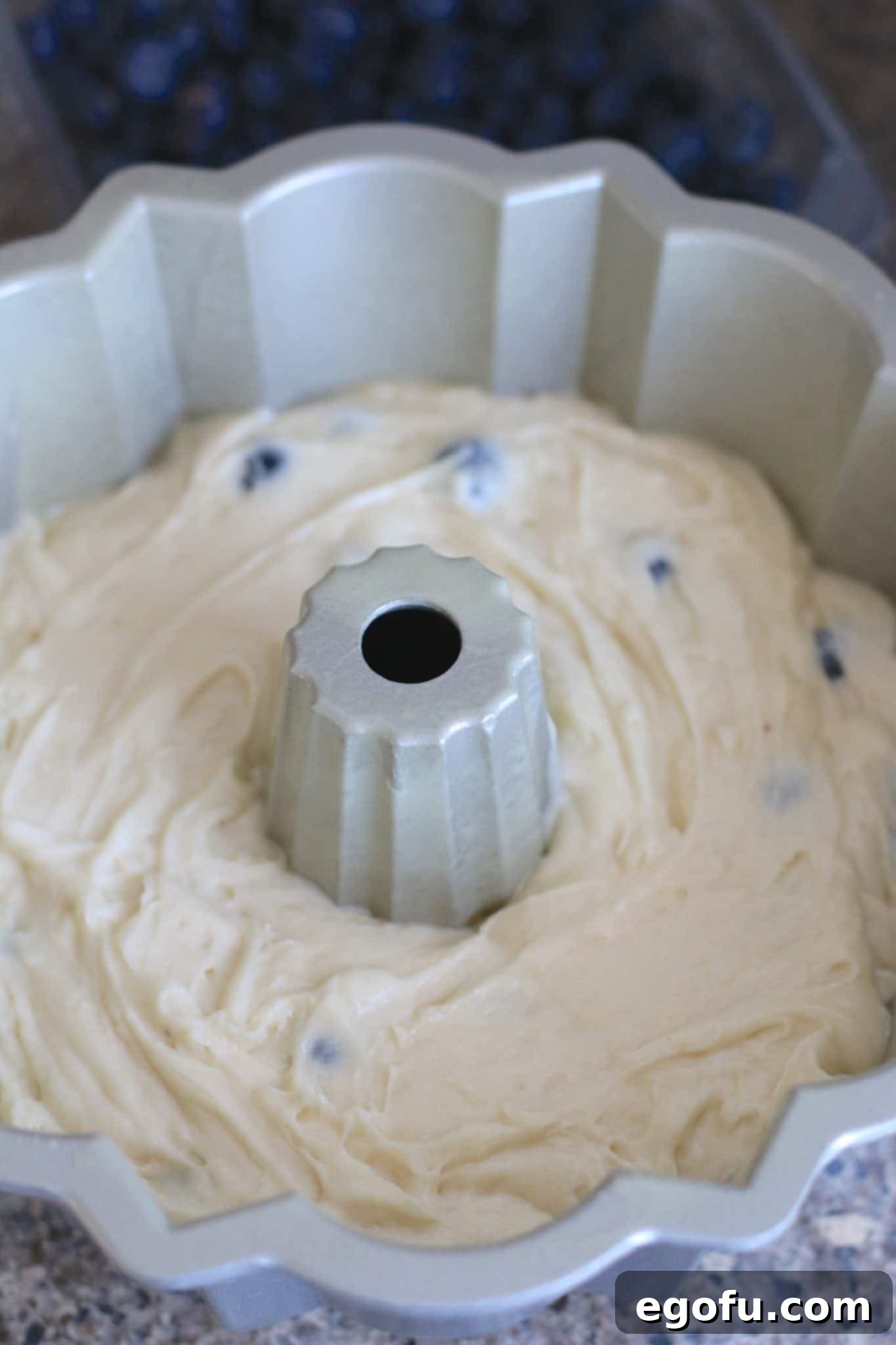 The vibrant blueberry cake batter, studded with fresh blueberries, has been meticulously poured into a bundt pan, ready for baking.