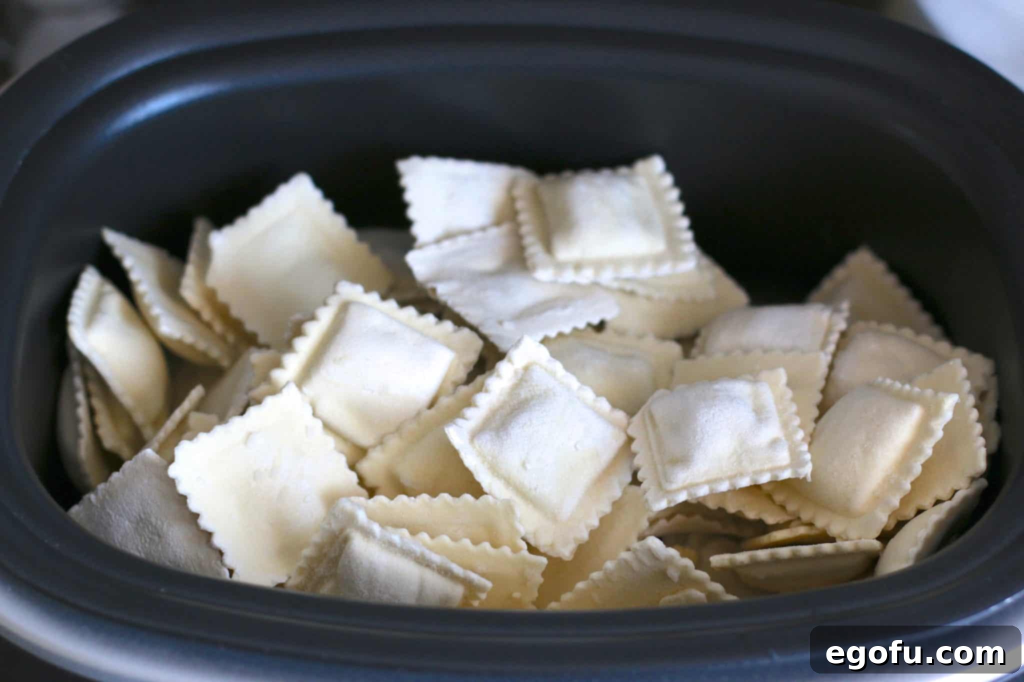 Frozen ravioli filling the bottom of a Ninja slow cooker, ready for the sauce.