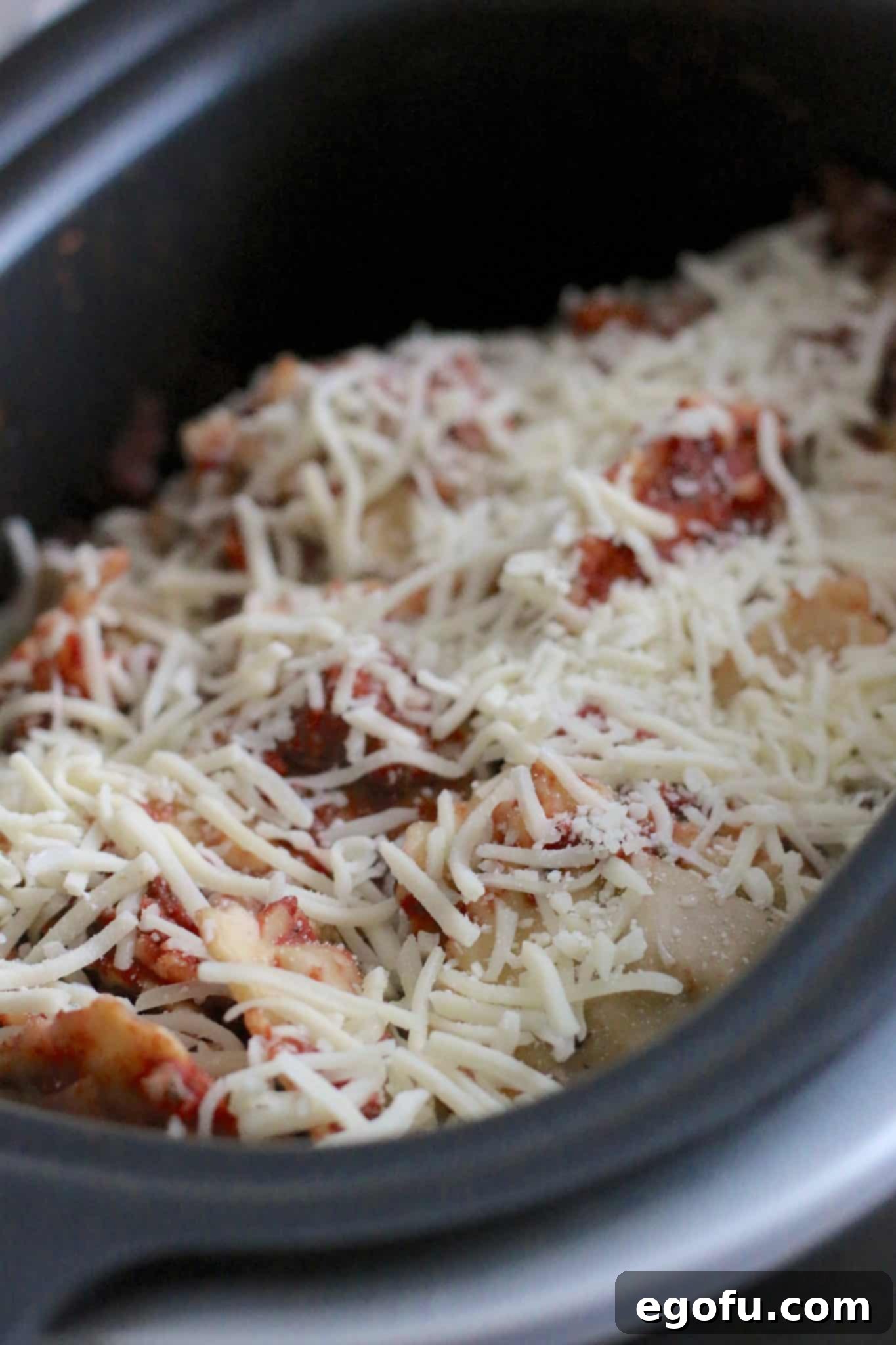 Cooked ravioli, marinara sauce, and shredded mozzarella cheese in an oval Ninja slow cooker just before the cheese melts.